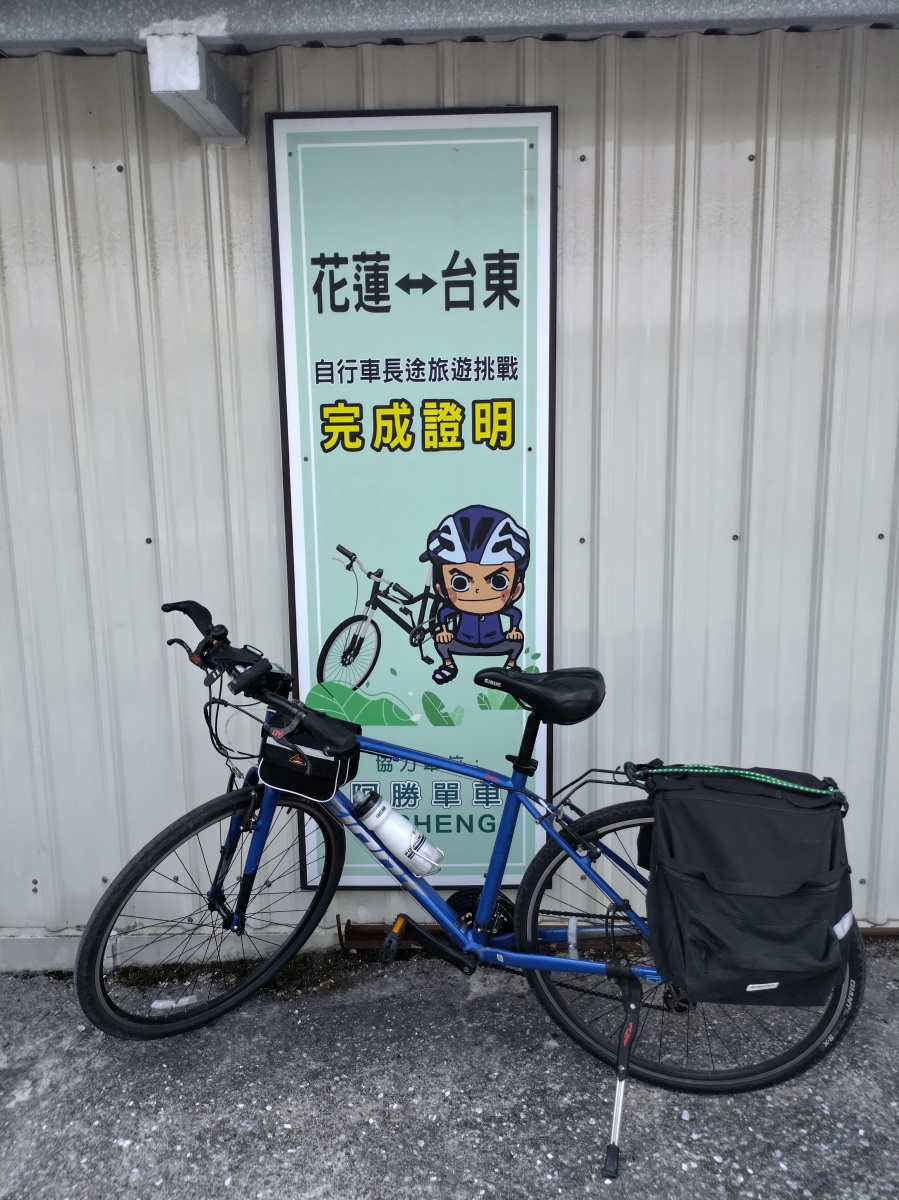 Blue giant bicycle with black panniers in front of a sign for A-sheng bike hire in Hualien