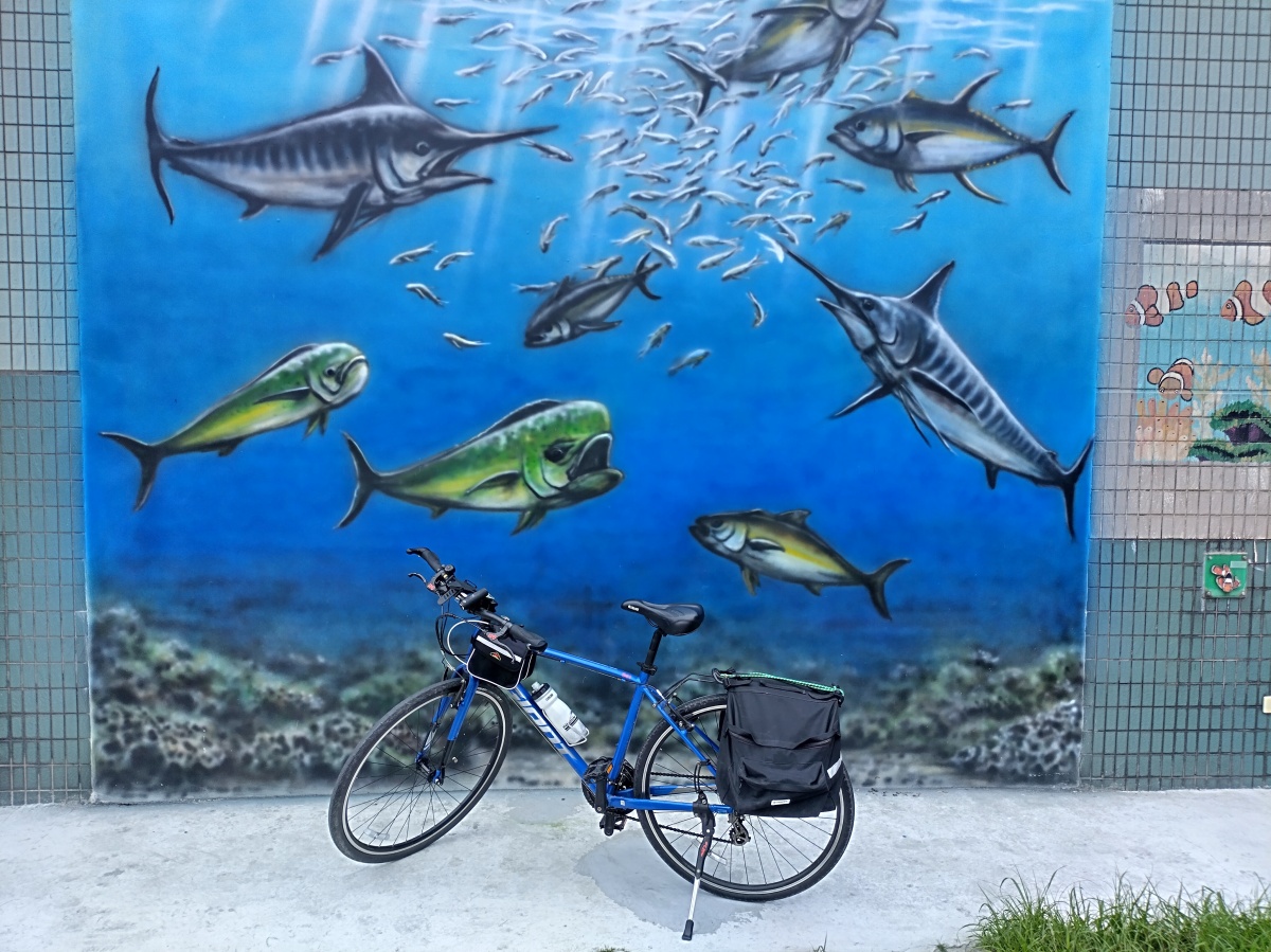 Blue Giant bicycle in front of a mural depicting an underwater scene of fish swimming
